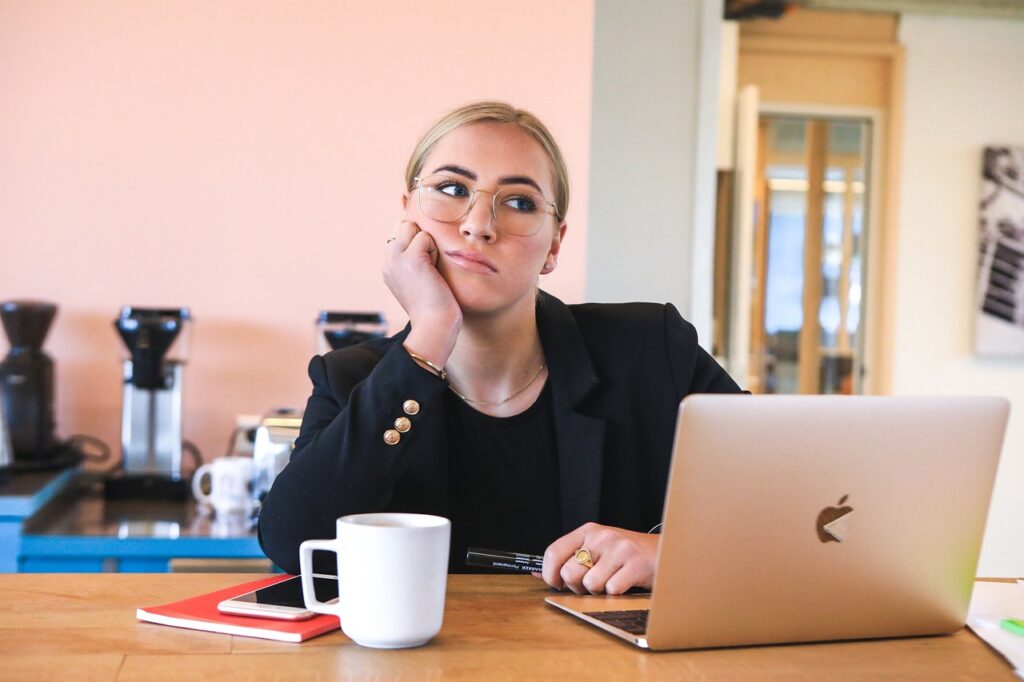 A bored women sitting at a table with her laptop.